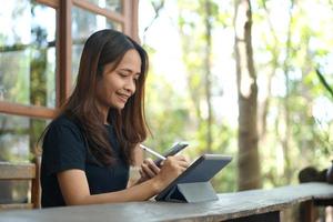 les femmes asiatiques sont heureuses de s'asseoir et de travailler dans un café. il y a des arbres verts entourés par la nature. la planification d'entreprise est une bonne idée. photo