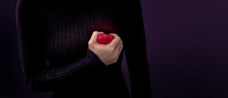 douloureux, concept de crise cardiaque. jeune femme serra un cœur en plastique rouge contre sa poitrine. maladie cardiaque ou sentiment de chagrin et de chagrin photo