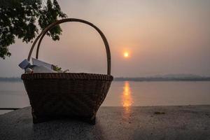 les étoffes dans un panier en osier pour offrir de la nourriture ou faire l'aumône aux moines sur une chaise en pierre au bord du mékong, en thaïlande à l'heure du lever du soleil. photo