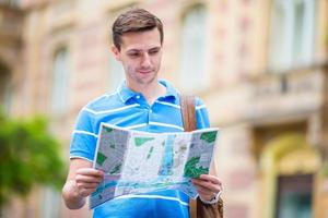 jeune homme cherchant dans la rue avec un plan de ville en europe. touriste caucasien regardant la carte de la ville européenne à la recherche d'attractions. photo