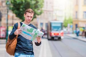 jeune homme à lunettes de soleil avec un plan de la ville et un sac à dos en europe. touriste caucasien regardant la carte de la ville européenne à la recherche d'attractions. photo