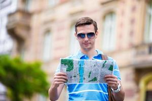 jeune homme à lunettes de soleil avec un plan de la ville et un sac à dos en europe. touriste caucasien regardant la carte de la ville européenne à la recherche d'attractions. photo