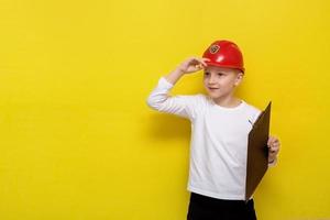 garçon dans un casque de construction avec une tablette dans ses mains sur un fond jaune avec espace de copie photo