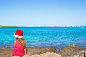 vue arrière de l'adorable petite fille en bonnet de noel sur une grosse pierre photo