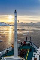 les gens sur le pont du navire regardant le coucher du soleil parmi les icebergs dérivant au canal lemaire, antarctique photo