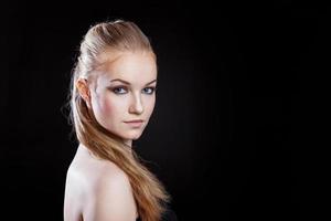 fille de modèle de mode de beauté avec une longue coiffure en queue de cheval de cheveux lisses et sains sur fond noir. souriante jolie femme regardant la caméra. parfait portrait de peau fraîche. concept de jeunesse et de soins de la peau. photo