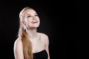 fille de modèle de mode de beauté avec une coiffure en queue de cheval de longs cheveux lisses et sains sur fond noir. souriante jolie femme regardant la caméra. parfait portrait de peau fraîche. concept de soins de la jeunesse et de la peau. photo