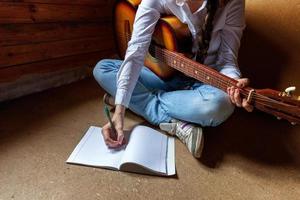 jeune femme hipster assise sur le sol et jouant de la guitare à la maison. adolescente apprenant à jouer de la chanson et à écrire de la musique dans sa chambre. passe-temps, mode de vie, détente, instrument, loisirs, concept d'éducation. photo