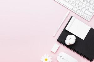 table de bureau minimaliste avec ordinateur clavier, souris, stylo blanc, fleurs de coton, gomme sur une table pastel rose avec espace de copie pour saisir votre texte, composition du lieu de travail de couleur rose, pose à plat, vue de dessus photo