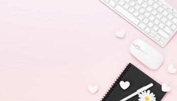 table de bureau minimaliste avec trombone coeur, ordinateur clavier, souris, stylo blanc, fleurs de coton, gomme sur une table pastel rose avec espace de copie pour saisir votre texte, concept de la Saint-Valentin, pose à plat, vue de dessus photo