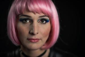 portrait de jeune fille sur fond noir avec perruque rose et lentilles colorées photo