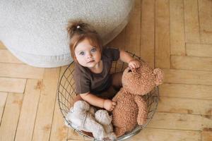 portrait de jolie petite fille assise dans un panier avec des peluches à la maison photo
