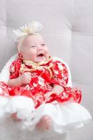 gros plan mignon bébé nouveau-né en body rouge allongé seul sur le lit. adorable bébé repose sur des draps blancs, regardant la caméra à l'air paisible. petite enfance, soins de santé et pédiatrie, concept de petite enfance. photo