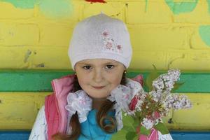 biélorussie, ville de gomil, 16 mai 2016. une belle petite fille dans un bonnet tricoté tient un brin de lilas et sourit. photo