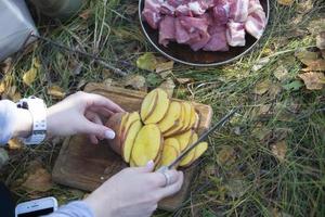 couper les pommes de terre pour les grillades en plein air. les mains de la femme coupent une pomme de terre avec un couteau pour un barbecue. photo