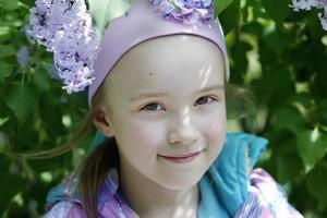 biélorussie, ville de gomil, 16 mai 2016. rue de la ville. une belle petite fille se tient près d'un buisson de lilas et sourit. photo