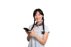 portrait d'heureuse belle jeune femme asiatique en robe denim à l'aide d'un smartphone sur fond blanc. tourné en studio photo