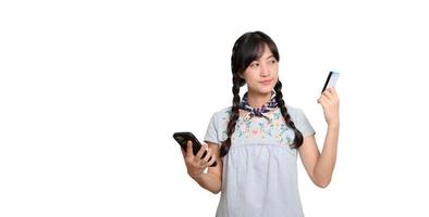 portrait d'une belle jeune femme asiatique heureuse en robe denim tenant une carte de crédit et un smartphone sur fond blanc. tourné en studio photo