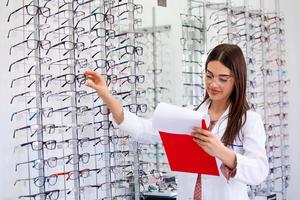 jolie ophtalmologiste écrivant des données dans un presse-papiers, travaillant dans un magasin d'optique. concept de soins de santé et de médecine photo