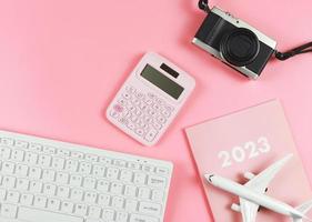 mise à plat du clavier d'ordinateur blanc, journal rose 2023, modèle d'avion, calculatrice rose et appareil photo sur fond rose avec espace de copie. concept de planification de voyage.