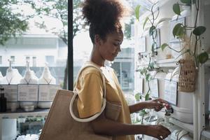 une cliente afro-américaine remplit du savon liquide dans une bouteille de recyclage à partir de contenants réutilisables dans un magasin zéro déchet et de recharges, un magasin de détail respectueux de l'environnement et un mode de vie d'achat durable. photo