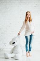 fille enceinte rousse dans un chemisier léger et un jean bleu avec un ours en peluche photo