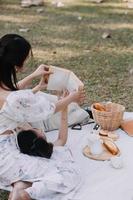 jeunes jolies filles jumelles brunes assises sur l'herbe avec les jambes légèrement pliées aux genoux et regardant dans un livre brun, portant un manteau décontracté par temps ensoleillé d'automne sur fond flou. photo