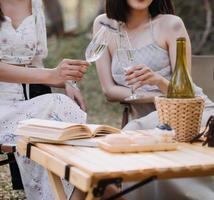 jeunes jolies filles jumelles brunes assises sur l'herbe avec les jambes légèrement pliées aux genoux et regardant dans un livre brun, portant un manteau décontracté par temps ensoleillé d'automne sur fond flou. photo