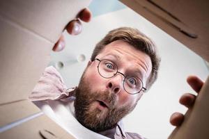 l'homme a déballé un colis livré, regarde le contenu avec une expression surprise et drôle. déballage vue intérieure. fermer. photo