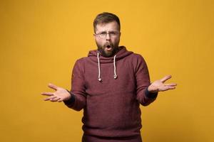 un homme barbu mécontent et agacé avec des lunettes lève les mains dans la confusion et dit quelque chose en regardant la caméra. photo