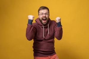 un homme caucasien heureux fait un geste gagnant, il lève énergiquement les poings et crie de joie. fond jaune. photo