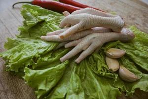 pattes de poulet crues sur une planche à découper avec de la laitue, des piments rouges et de l'ail. pieds de poulet frais et bio. vue de dessus photo