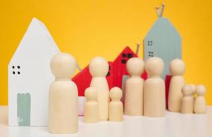 maison en bois et figurines miniatures d'une famille et d'un agent immobilier sur fond jaune. le concept de vente et d'achat de biens immobiliers, d'investissement photo