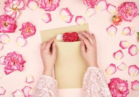 deux mains féminines mettent un coeur rouge dans une enveloppe en papier brun photo