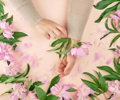 mains d'une jeune fille à la peau lisse et un bouquet de pivoines roses photo