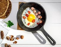 oeuf de poulet frit avec des morceaux de saucisse dans une poêle en fonte noire photo