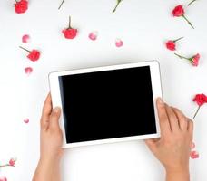 Tablette électronique blanche avec un écran noir vierge et deux mains féminines tenant un appareil sur fond blanc photo