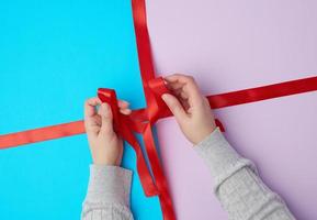 deux mains féminines attachent un arc avec un ruban rouge satiné sur une boîte cadeau photo