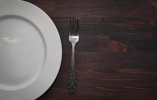 assiette blanche vide avec une fourchette sur une surface brune en bois photo