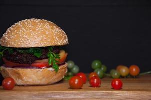 savoureux burger avec des escalopes de viande servi sur une planche de bois avec des tomates cerises photo