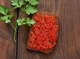 le caviar de saumon rouge repose sur un morceau de pain de seigle. table en bois marron photo
