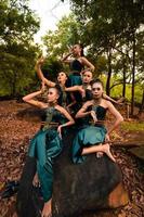 un groupe de personnes asiatiques en costumes verts assis sur un gros rocher avec des feuilles brunes en arrière-plan photo