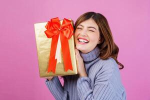 portrait d'une jeune femme surprise excitée tenant un cadeau dans ses mains isolée sur fond rose photo