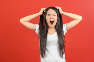 portrait de jeune femme asiatique frustrée et en colère en t-shirt blanc tirant ses cheveux isolé sur fond rouge photo