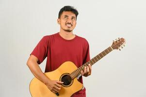 Portrait de jeune homme asiatique en t-shirt rouge jouant une guitare acoustique isolé sur fond blanc photo