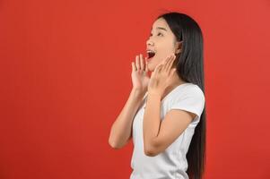 portrait de jeune femme asiatique en t-shirt blanc levant les yeux et excitant isolé sur fond rouge photo