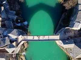 vue aérienne par drone du vieux pont de la ville de mostar en bosnie-herzégovine pendant la journée ensoleillée. couleurs bleu turquoise de la rivière neretva. Patrimoine mondial de l'UNESCO. personnes marchant sur le pont. photo