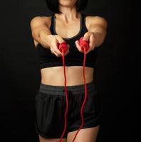 jeune femme avec une figure sportive en uniforme noir tient une corde rouge pour sauter photo