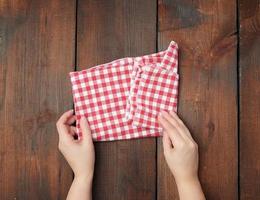 les mains tiennent une serviette de cuisine à carreaux rouge blanc sur un fond de bois marron photo