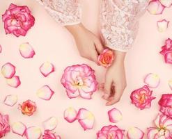 mains féminines à la peau lisse, fond blanc avec des boutons de rose roses photo